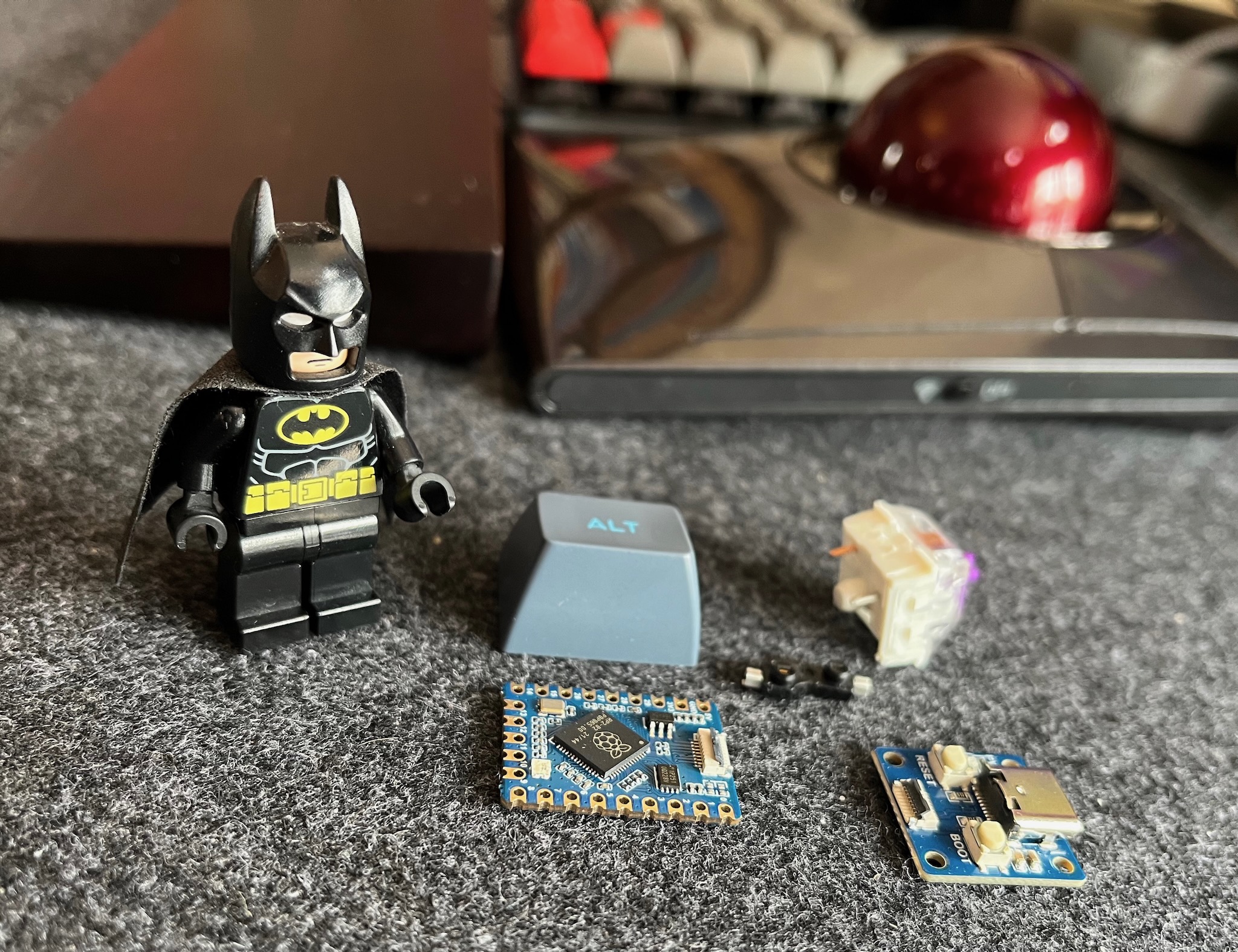 a picture of the waveshare rp2040-tiny microcontroller and usb boards, a kailh hotswap socket, a key switch, a blue alt keycap, and a batman lego minifigure for scale (this is the article's hero image)